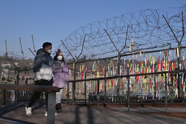 Visitors walk past a military fence decorated with ribbons wishing for peace and reunification of the Korean Peninsula at the Imjingak peace park near the Demilitarized zone (DMZ) dividing the two Koreas in Paju on January 1, 2022