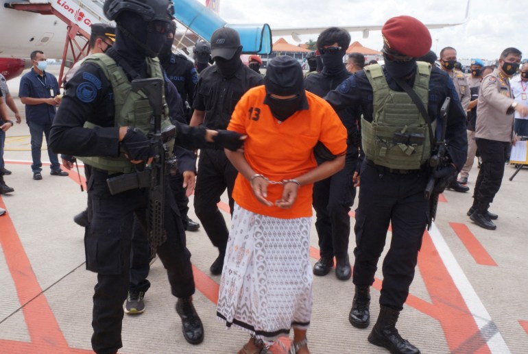 Zulkaernen in orange prison top and white sarong is escorted by armed police from a plane at Jakarta airport after his capture in December 2020