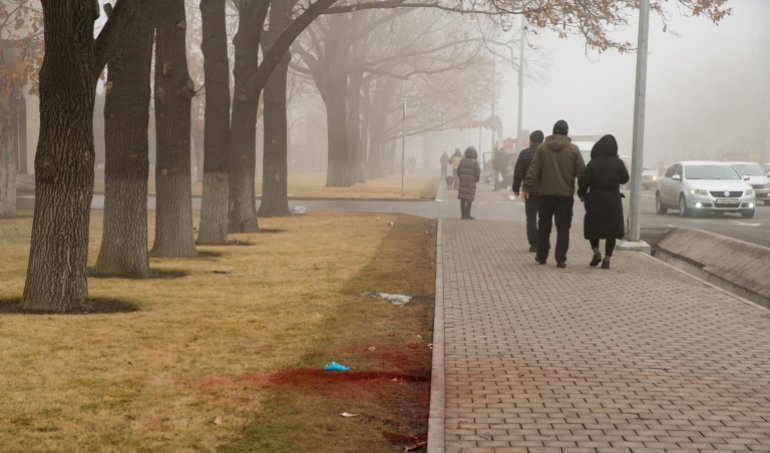 People walk past blood on a curbside lawn in central Almaty