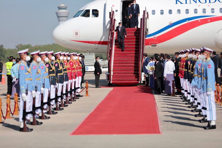 Hun Sen descends the stairs of his plane on the runway of Naipido Airport to a red carpet and a guard of honor by soldiers dressed in pale blue tops and white pants