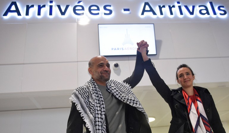 الناشط المصري الفلسطيني رامي شعث يرفع ذراع زوجته سيلين ليبرون شعث لدى وصوله إلى مطار رويسي في مدينة رواسي ، خارج باريس ، في 8 يناير 2022.