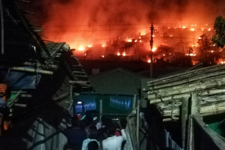 Gli spettatori si radunano mentre fumo e fiamme possono essere visti su una collina dopo lo scoppio di un incendio in un campo Rohingya