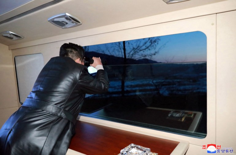 Kim looks through binoculars at a window