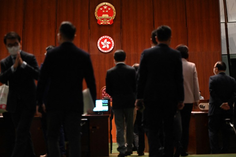 New members of Hong Kong's legislature stand on front of emblems from China and Hong Kong affixed to the wall 
