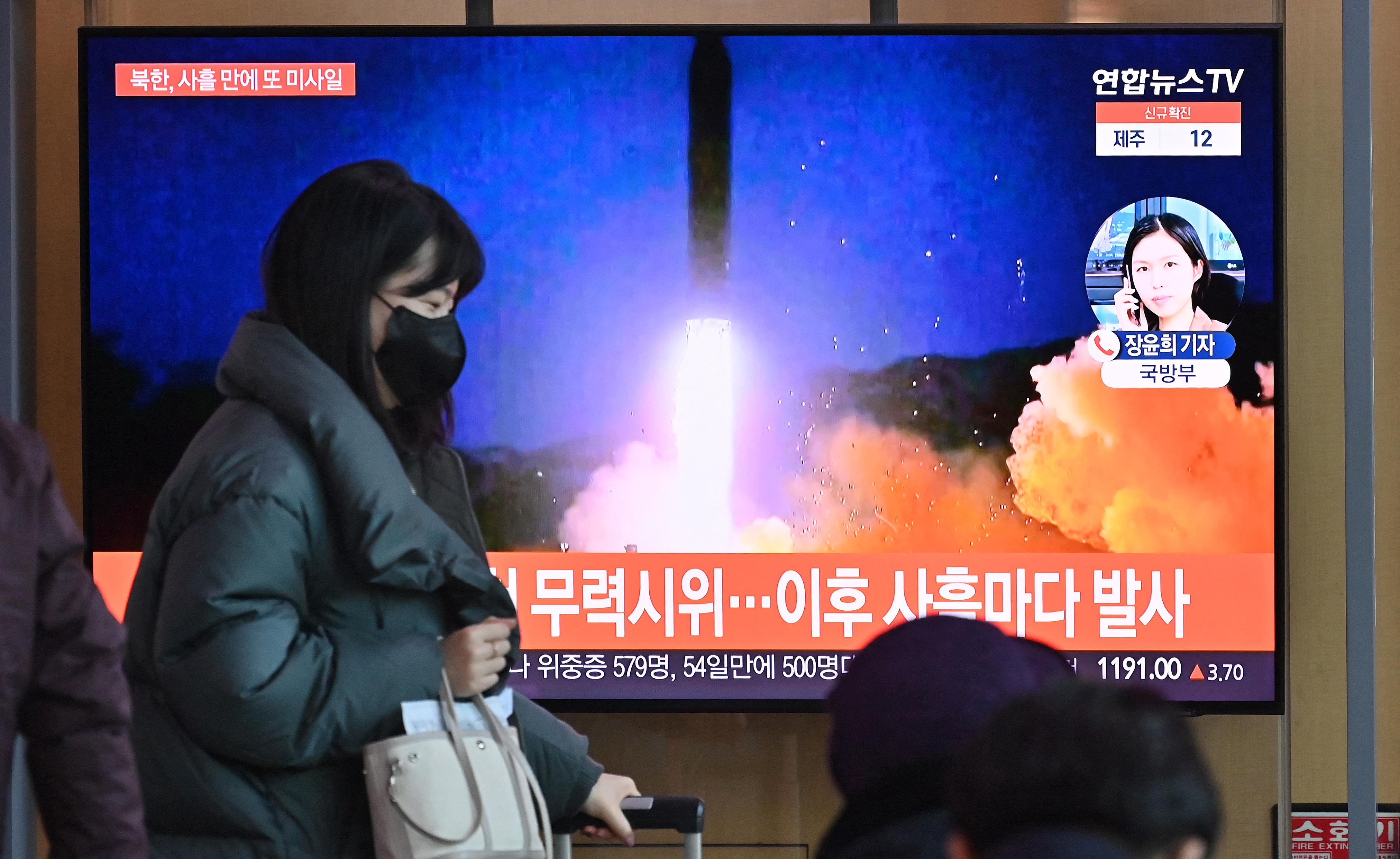 Uma mulher passa por uma tela de televisão mostrando um noticiário com imagens de arquivo de um teste de míssil norte-coreano, em uma estação ferroviária em Seul em 17 de janeiro de 2022, depois que a Coreia do Norte disparou um projétil não identificado para o leste no quarto teste de armas suspeito do país este mês segundo os militares do Sul.