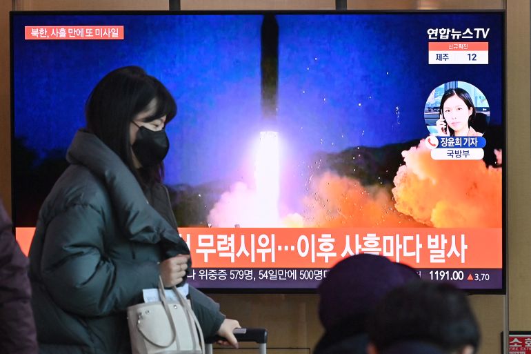A woman walks past a television screen showing a news broadcast with file footage of a North Korean missile test, at a railway station in Seoul on January 17, 2022, after North Korea fired an unidentified projectile eastward in the country's fourth suspected weapons test this month according to the South's military.