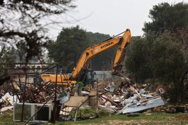 Israeli forces stand guard as machinery clean the ruins of the Palestinian Salhiya family's house, in the Sheikh Jarrah