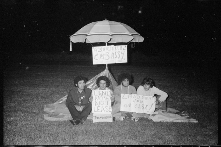A black and white photo from 1972 showing the Aboriginal Embassy under a beach umbrella. Left to right: Michael Anderson, Billy Craigie, Bert Williams and Tony Coorey.