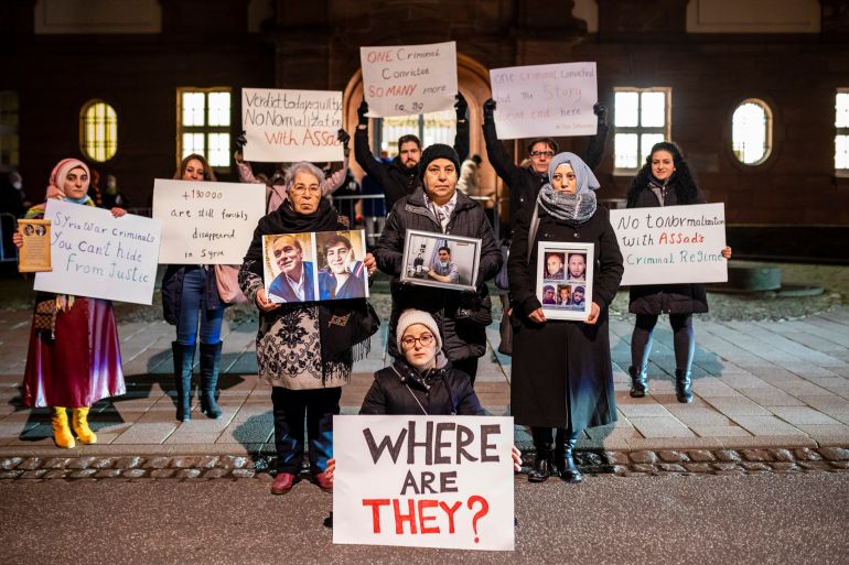 Syrian activists pose with banners in front of the court in Koblenz, Germany on January 13, 2022