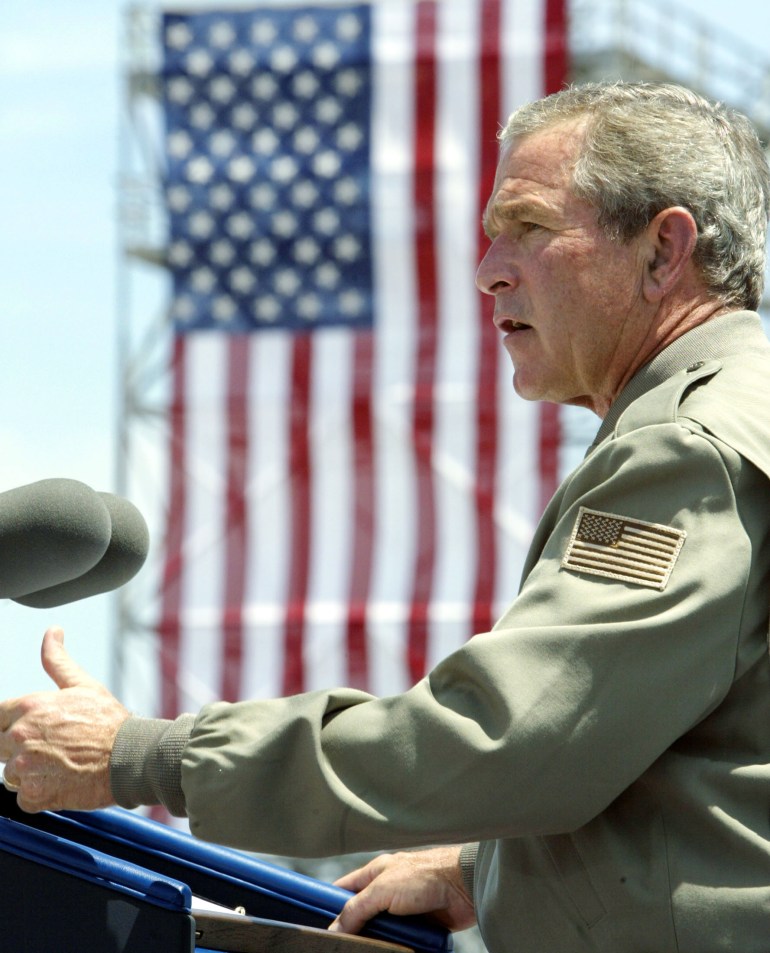 جورج دبلیو بوش، رئیس جمهور سابق آمریکا با لباس رسمی و در مقابل پرچم آمریکا از دستگیری همبالی استقبال کرد.