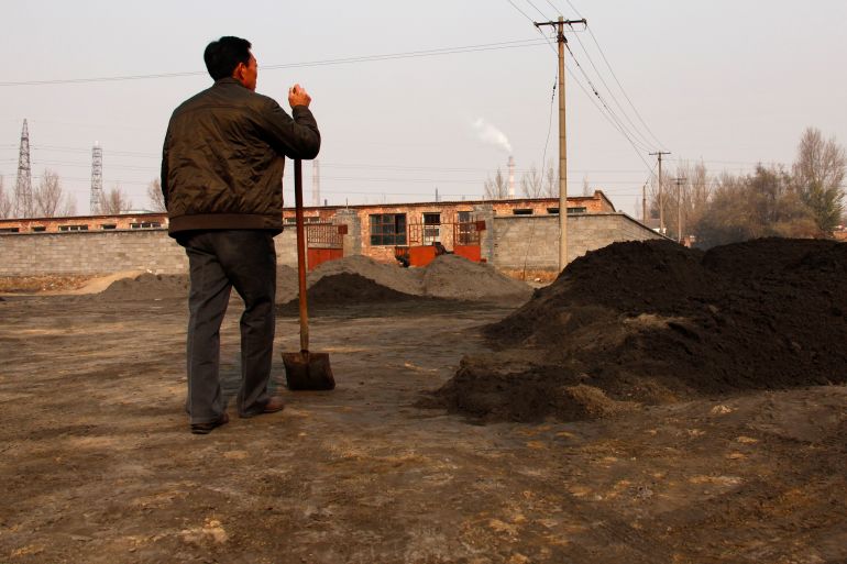 A villager looks towards a rare earth smelting plant as he takes a break from shovelling in China