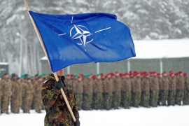 A soldier carries the NATO flag