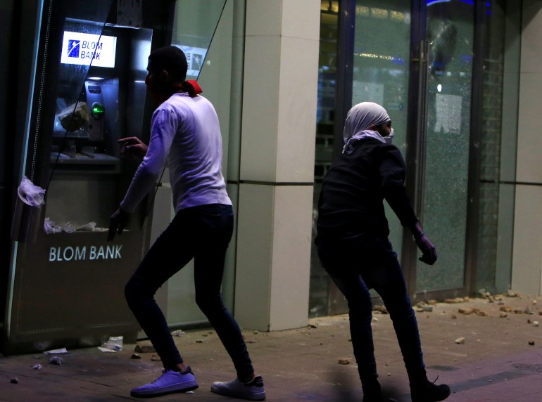 A protestor throws an object at an ATM machine of a bank during a protest against growing economic hardship in Sidon, Lebanon