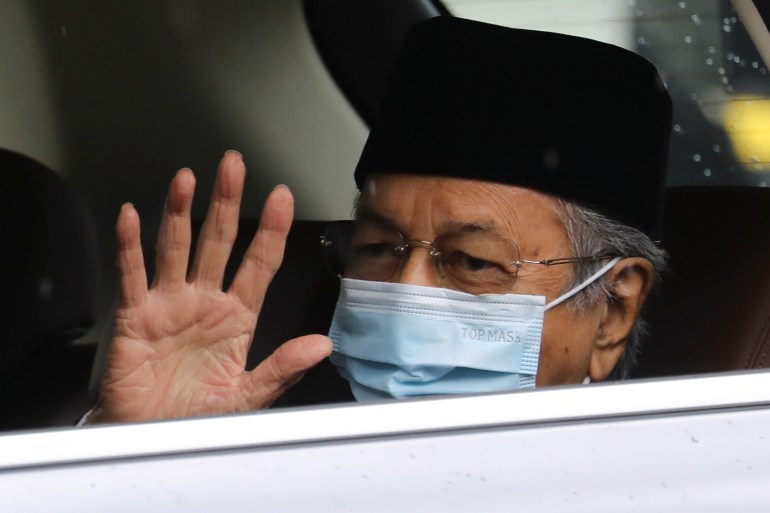 Malaysia's former Prime Minister Mahathir Mohamad, donning a mask, waves his right hand.