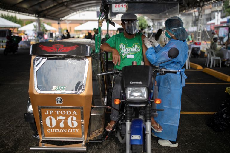 A health worker vaccinates a public transport driver with Sinovac COVID-19 vaccine in a shopping mall's parking lot turned into a drive-thru vaccination site, in Quezon City