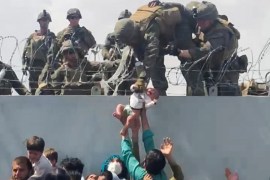 A baby is handed over to the American army over the wall of Kabul airport.