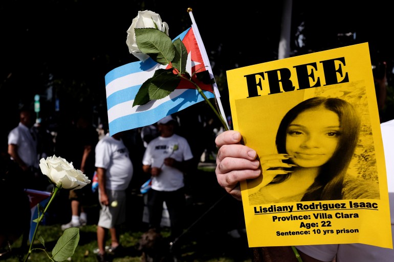 A man holding a white rose, a Cuban flag and a flyer showing a woman currently held in detention