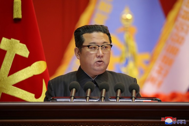 Kim Jong Un speaks at a conference in front of a red party flag