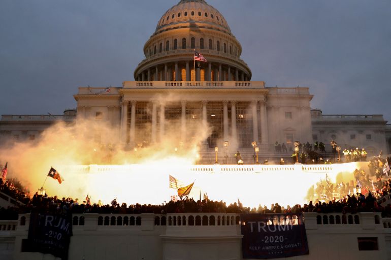 An explosion caused by a police munition illuminates supporters of former President Donald Trump rioting in front of the US Capitol Building one January 6, 2021.