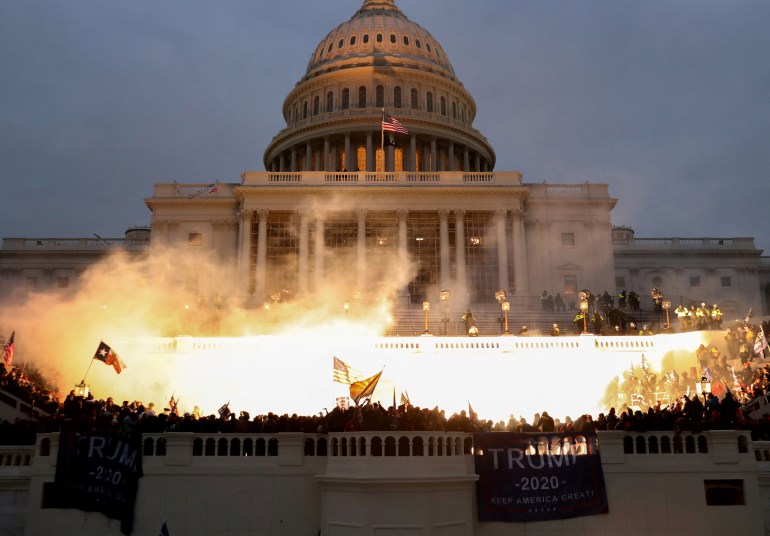 An explosion caused by a police munition illuminates supporters of former President Donald Trump rioting in front of the US Capitol Building one January 6, 2021.