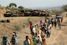 Villagers return from a market to Yechila town in south central Tigray walking past scores of burned vehicles, in Tigray, Ethiopia