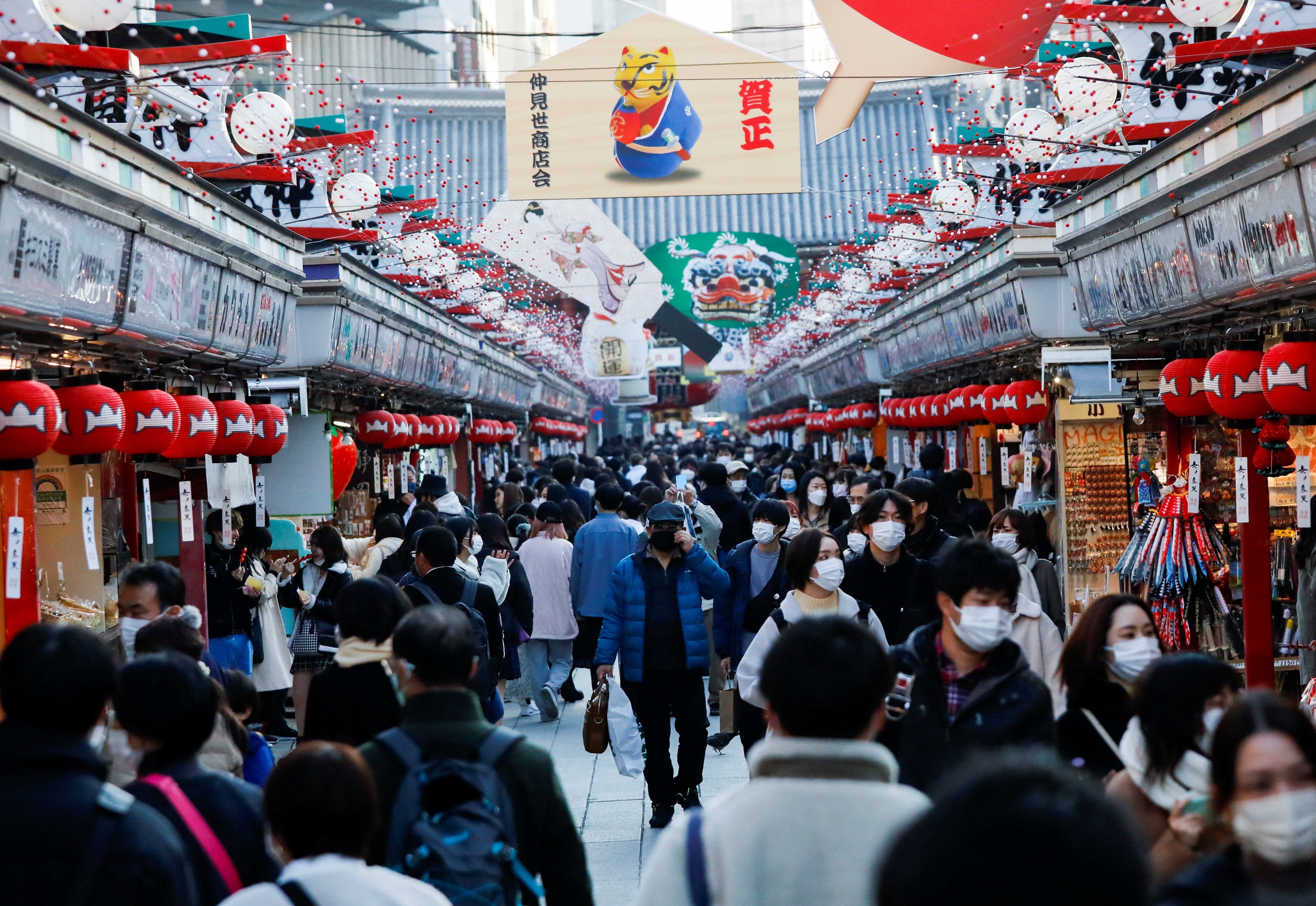 Visitantes usando máscaras protetoras caminham sob decorações para o Ano Novo na rua Nakamise que leva ao templo Senso-ji no distrito de Asakusa em meio à pandemia de COVID-19, em Tóquio