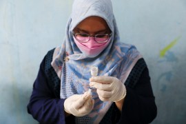 An Indonesian heathcare worker in a pale blue headscarf wearing disposable gloves prepares a dose of the Sinovac vaccine