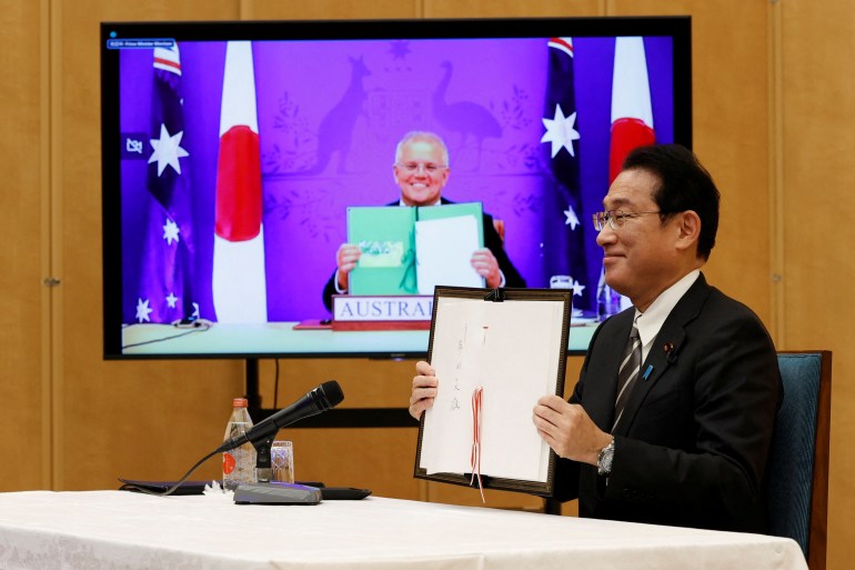 Japan's Prime Minister Fumio Kishida and Australia's Prime Minister Scott Morrison show off signed documents during their video signing ceremony of the bilateral reciprocal access agreement