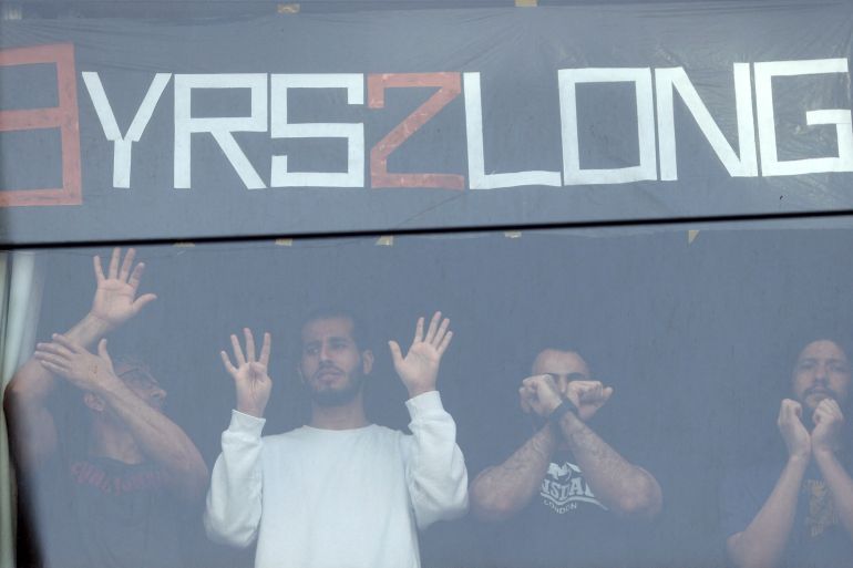 People standing in a window gesture toward pro-refugee protestors demonstrating outside the Park Hotel, where Serbian tennis player Novak Djokovic is believed to be held while he stays in Australia, in Melbourne