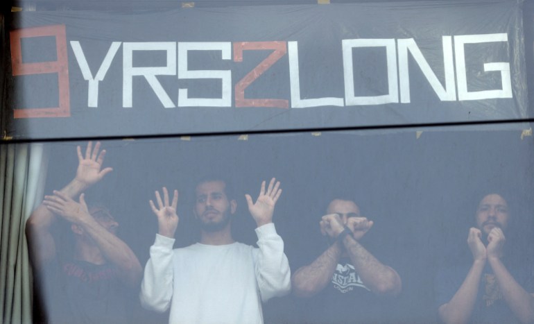 الناس يقفون في نافذة إيماءة تجاه المتظاهرين المؤيدين للاجئين الذين يتظاهرون خارج فندق بارك ، حيث يُعتقد أن لاعب التنس الصربي نوفاك ديوكوفيتش محتجز أثناء إقامته في أستراليا ، في ملبورن