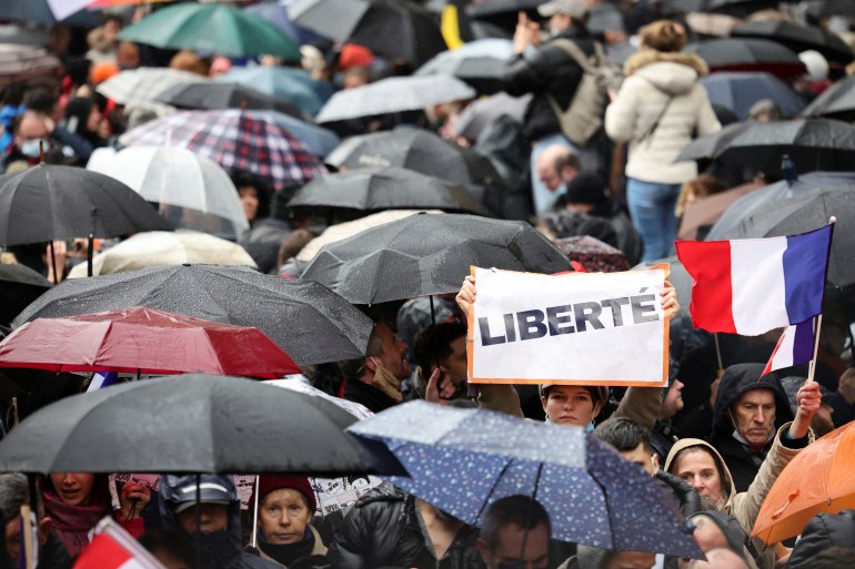 A person holds a sign that reads "Freedom" while people attend a rally to protest against a bill that would turn France's current COVID-19 health pass into a 