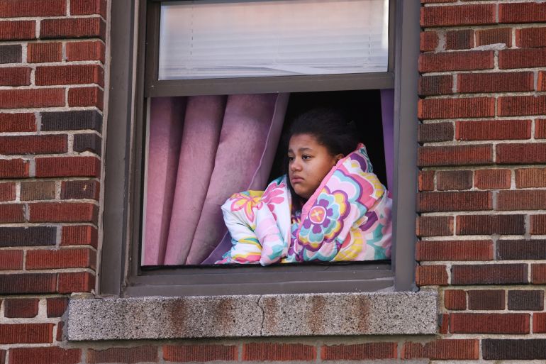 A woman wrapped in a blanket looking out of the window in the Bronx