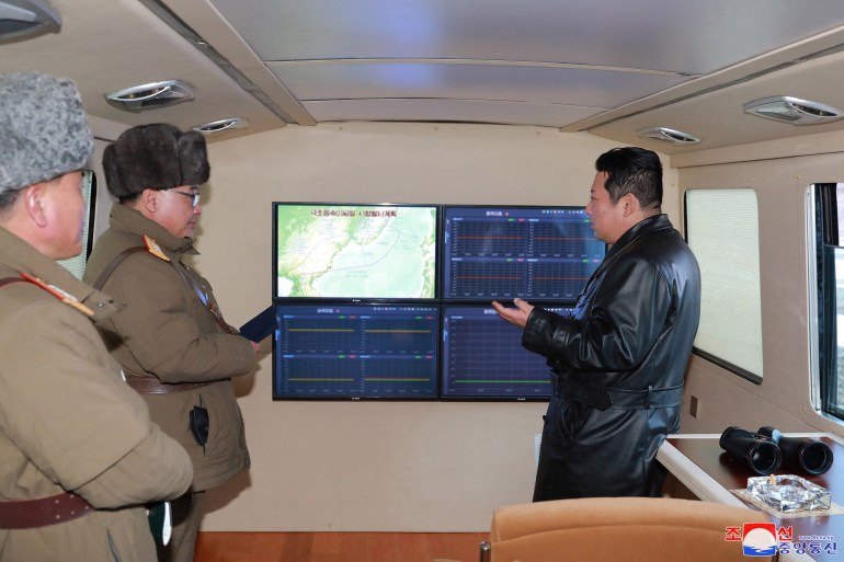 North Korean leader Kim Jong Un in a long black leather coat speaking to two officials as he supervises a hypersonic missile launch