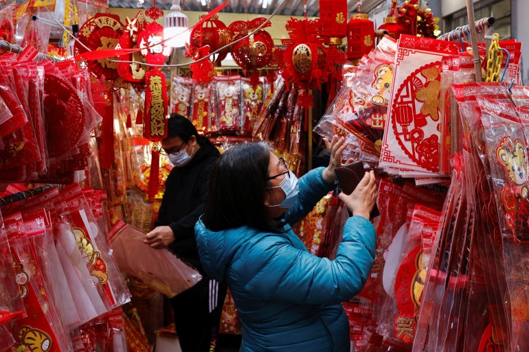 A woman in a blue coat looks through red and gold decorations for the Lunar New Year at a Hong Kong market