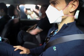 Novak Djokovic sits double-masked in a car departing the Park Hotel after his Australian visa was cancelled for a second time.