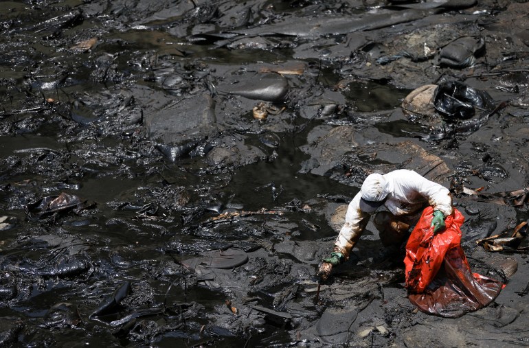 A worker clears up an oil spill caused by abnormal waves in Ventanilla, Peru