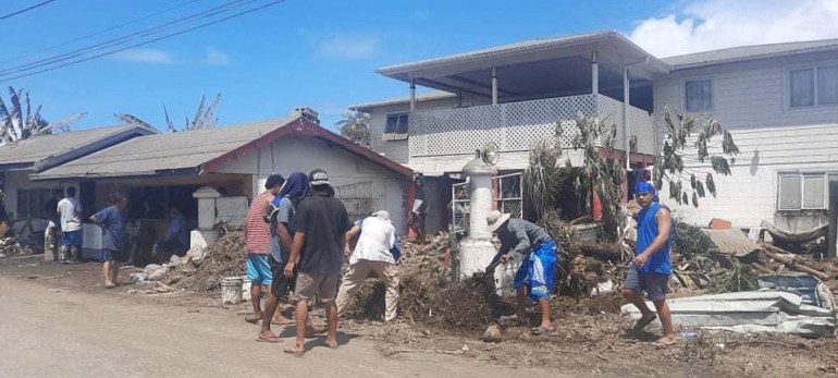 A group of people in Nuku'alofa kick rubbish in a heap on the street after Saturday's volcanic eruption and tsunami
