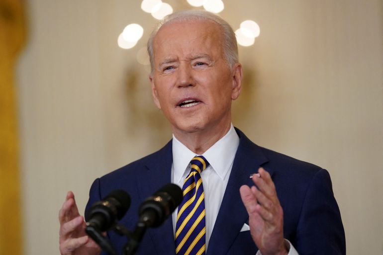 Joe Biden stands at a podium to deliver a speech on eve of one-year mark of his presidency