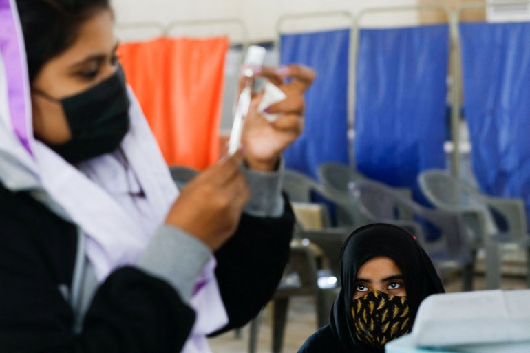 A girl in Karachi waits as a healthcare worker prepares a dose of COVID-19 vaccine