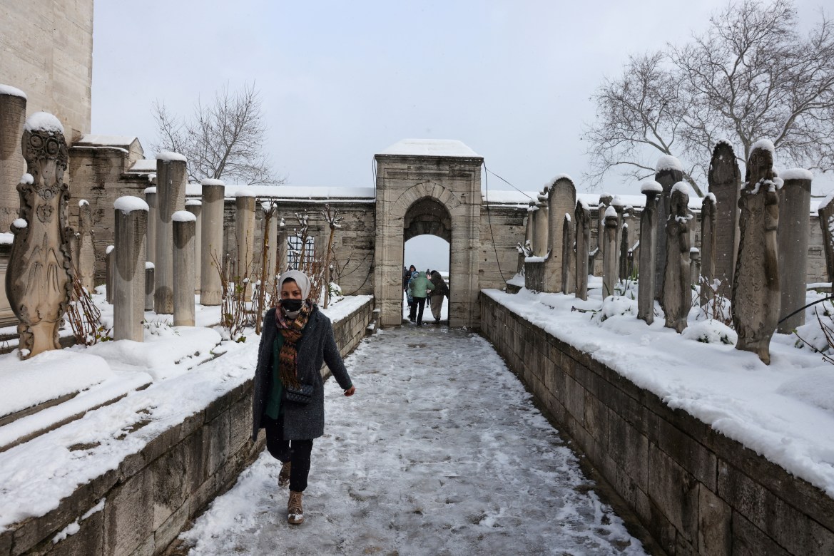 A woman walks through the cemetery of Suleymaniye Mosque during a snowy day in Istanbul,