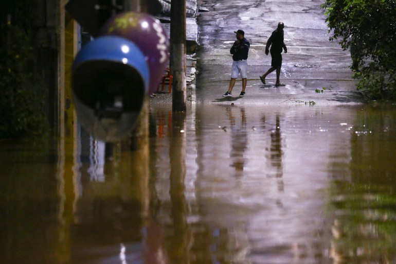 People stand in a flooded street after heavy rain in Caieiras, Brazil