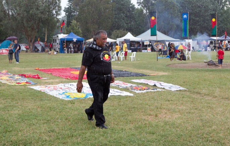 Ghillar Michael Anderson walks across the grass outside the Aboriginal Tent Embassy.