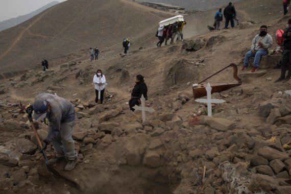 A cemetery worker shovels dirt into a grave that contains the remains of Apolonia Uanampa who died from the new coronavirus, as the coffin that contains the remains of Demetria Huamani, also a victim of the virus, is carried to her burial site at the Nueva Esperanza cemetery on the outskirts of Lima, Peru,