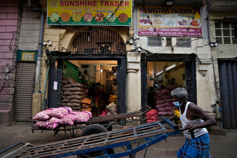 A Sri Lankan laborer pushes his cart past shops selling vegetables at a wholesale market