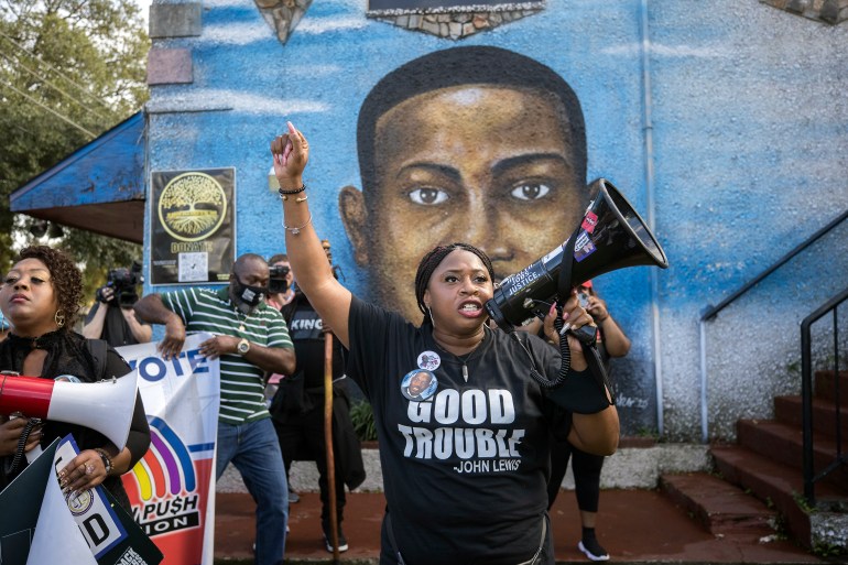 A civil rights activist shouts into a megaphone in front of a mural of Ahmaud Arbery