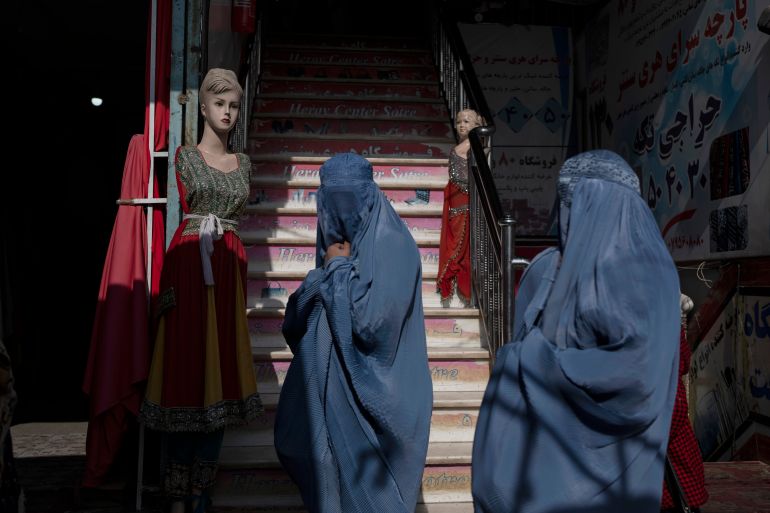 Burqa-wearing Afghan women walk past a clothing shop, in Herat