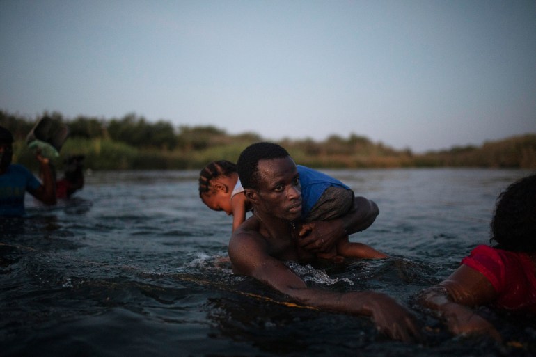 Migrant walking through river while carrying child