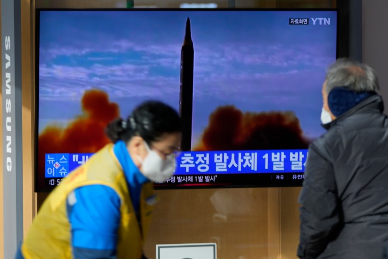 People in masks in front of a television screen showing a news update on North Korea's latest suspected missile launch