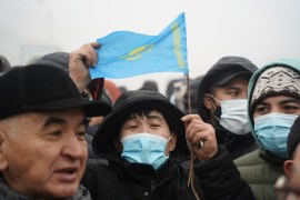 A Kazakh man holds up a flag of Kazakhstan amid a crowd of protesters