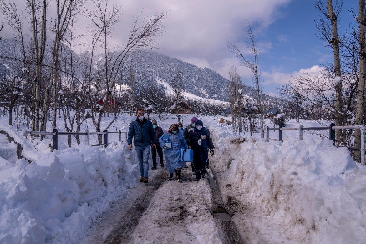 Team of healthcare workers and doctors carry vaccines as they walk on a snow covered road in Indian controlled Kashmir